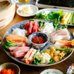 A temaki hand roll sushi spread on the dining table, consisting of plates and bowls containing sushi rice, sashimi, vegetable fillings, and nori seaweed.