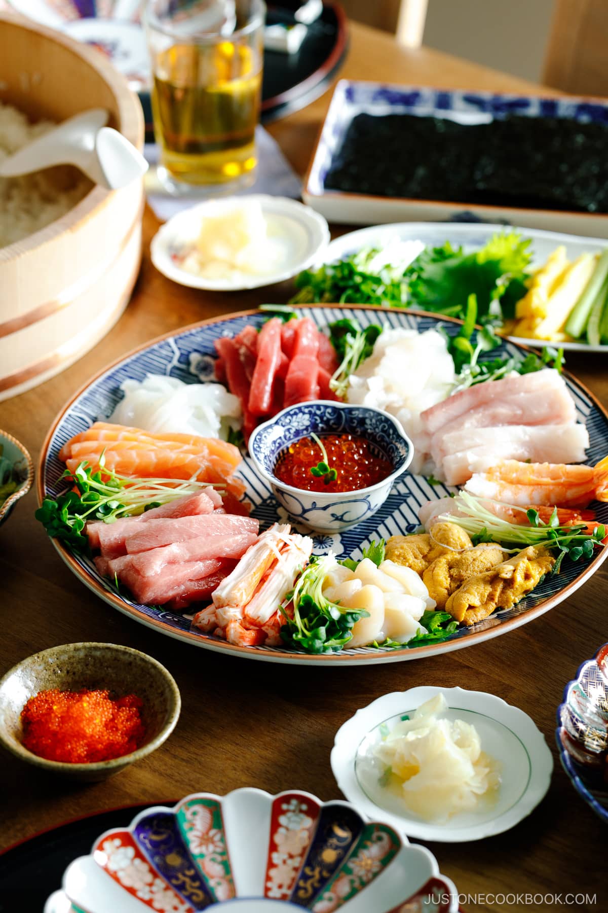 A temaki hand roll sushi spread on the dining table, consisting of plates and bowls containing sushi rice, sashimi, vegetable fillings, and nori seaweed.