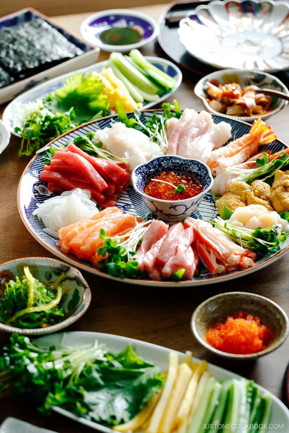 A temaki hand roll sushi spread on the dining table, consisting of plates and bowls containing sushi rice, sashimi, vegetable fillings, and nori seaweed.