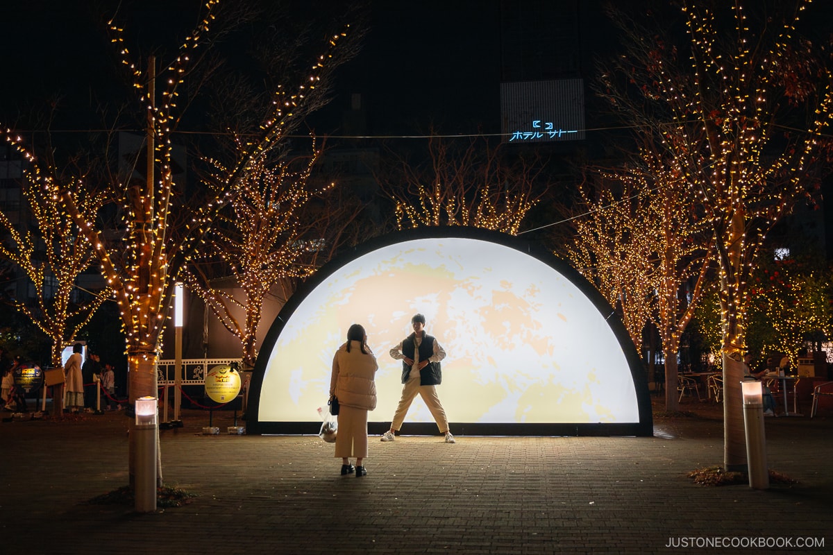 Person posing in front of illuminated half moon installation.