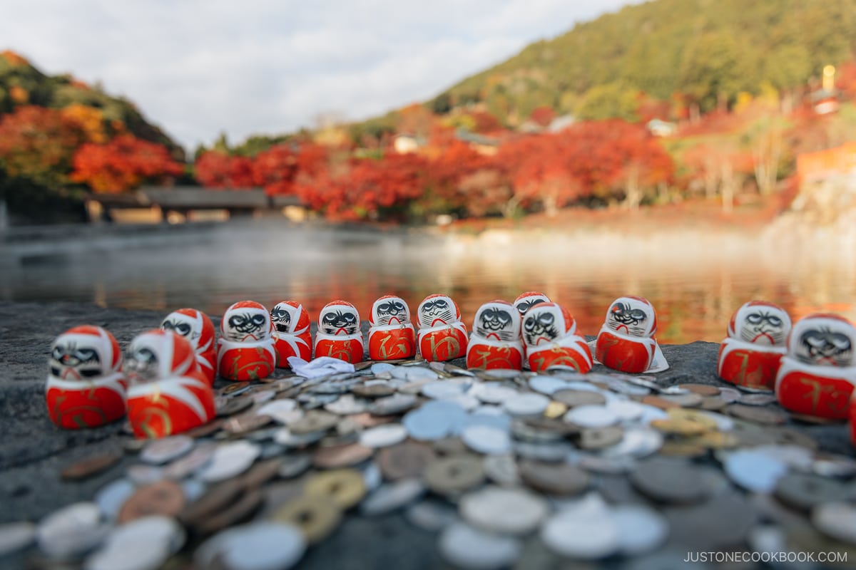 Japanese yen coins and small daruma dolls in front of a pond