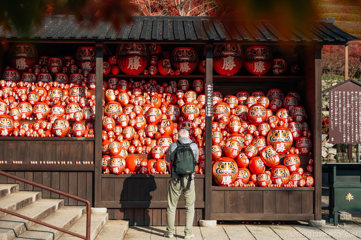 Man standing in front of a collection of red daruma dolls