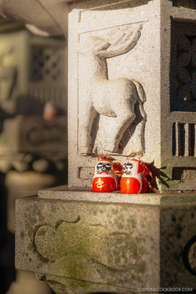 Two red Daruma dolls on a stone lantern