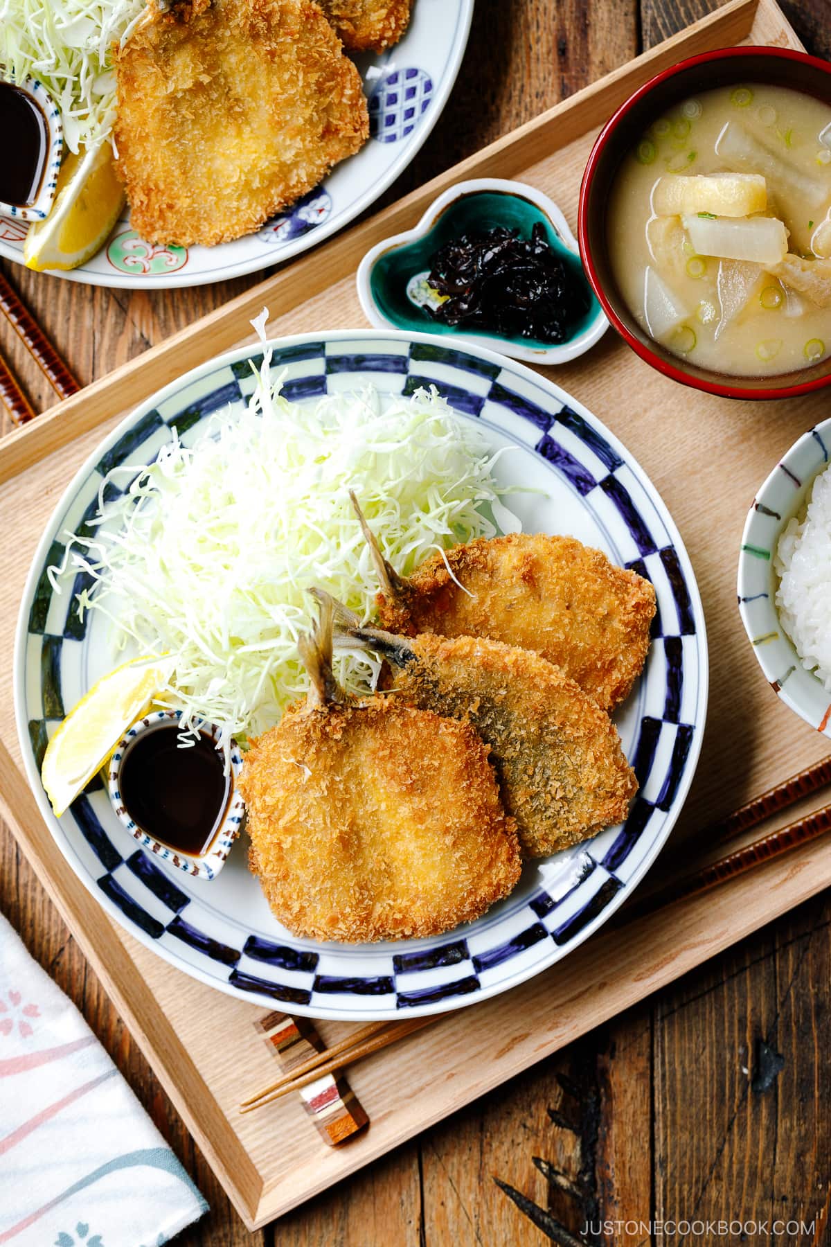 A plate containing panko-coated, fried horse mackerel fillets and a bed of shredded cabbage salad.