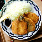 A plate containing panko-coated, fried horse mackerel fillets and a bed of shredded cabbage salad.