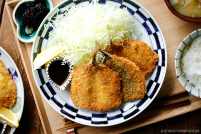 A plate containing panko-coated, fried horse mackerel fillets and a bed of shredded cabbage salad.