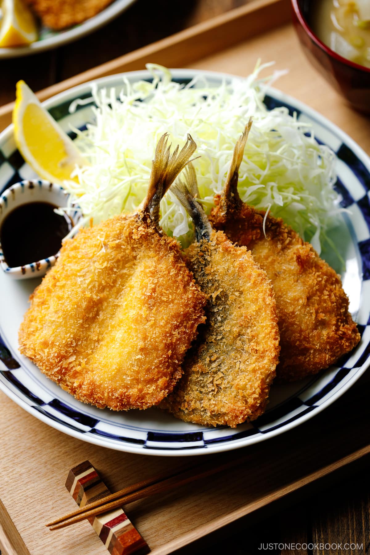 A plate containing panko-coated, fried horse mackerel fillets and a bed of shredded cabbage salad.