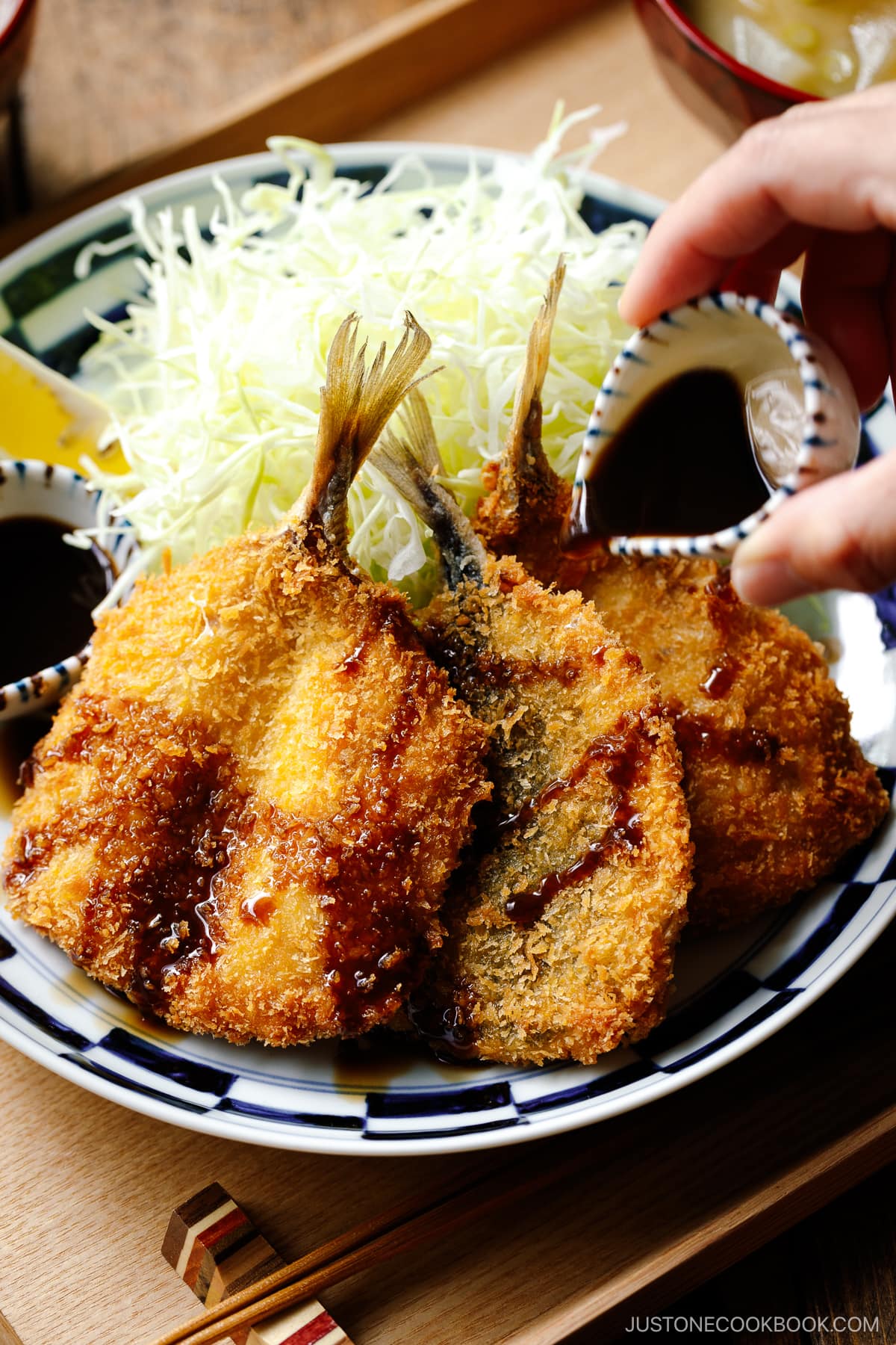 A plate containing panko-coated, fried horse mackerel fillets and a bed of shredded cabbage salad.