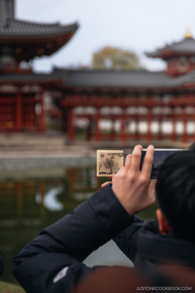 Person holding a 10,000 yen note in front of a temple