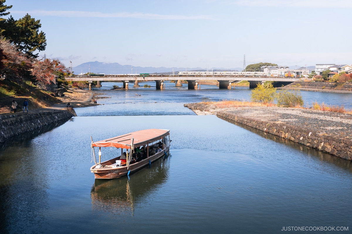 Woden boat on a river with a bridge and train in the background.