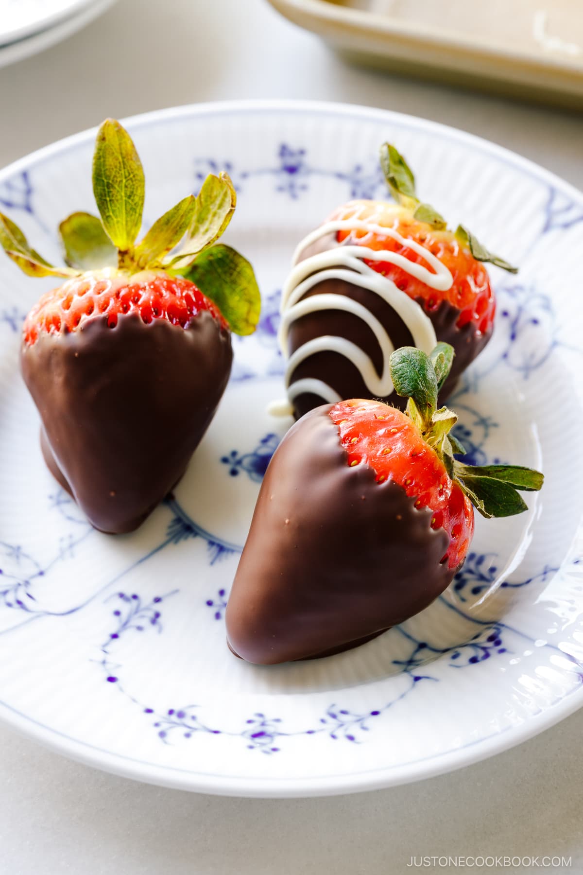 Three homemade chocolate covered strawberries on a Royal Copenhagen plate.