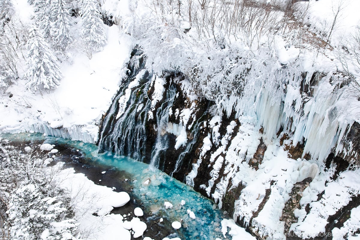 Frozen waterfall covered in snow and a blue river at the bottom