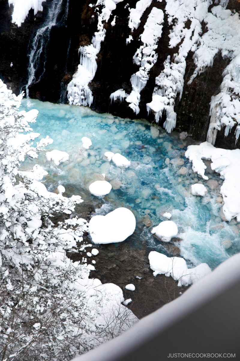 Frozen waterfall covered in snow and a blue river at the bottom