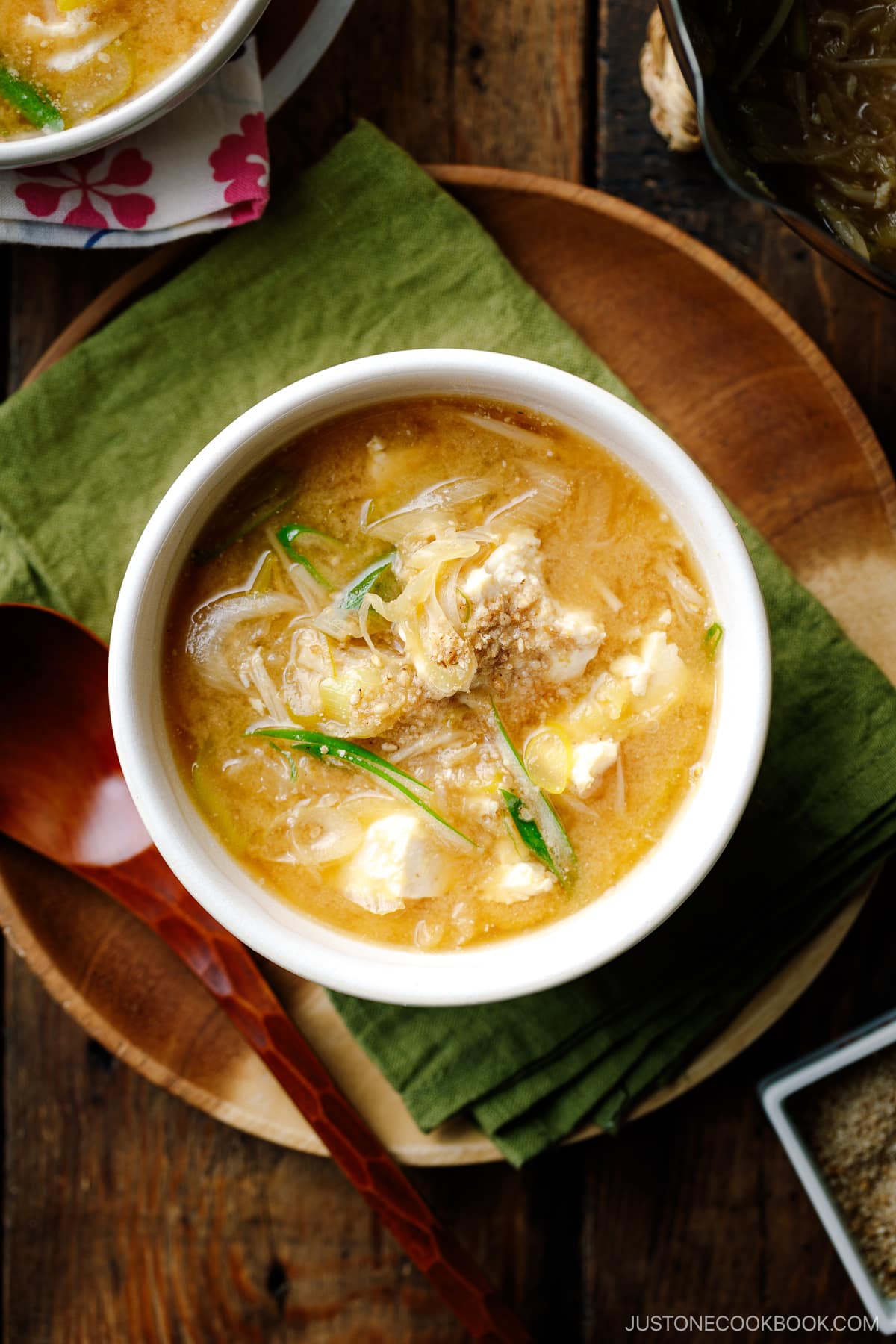 A white ceramic bowl containing Miso Soup with enoki mushrooms, tofu, and Japanese long green onion, topped with ground sesame seeds.