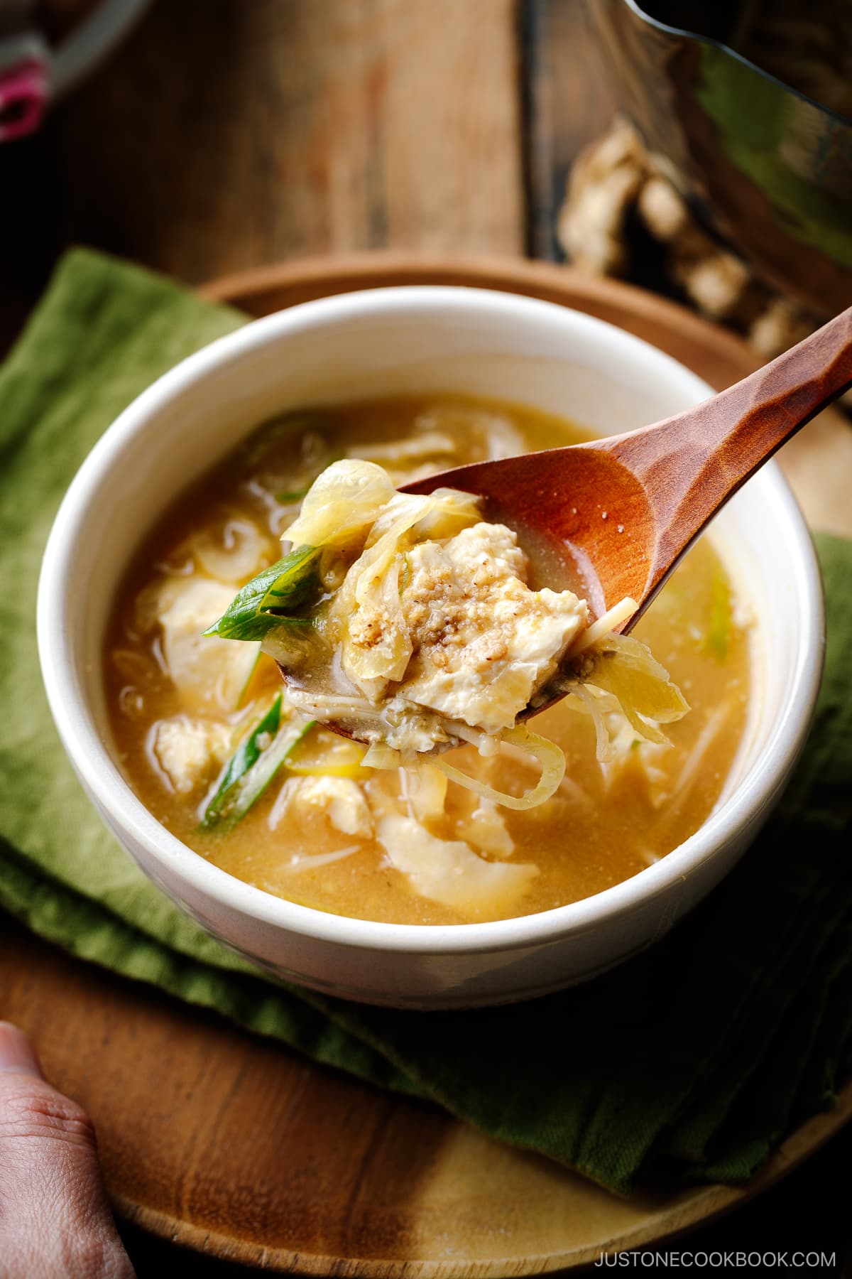 A white ceramic bowl containing Miso Soup with enoki mushrooms, tofu, and Japanese long green onion, topped with ground sesame seeds.