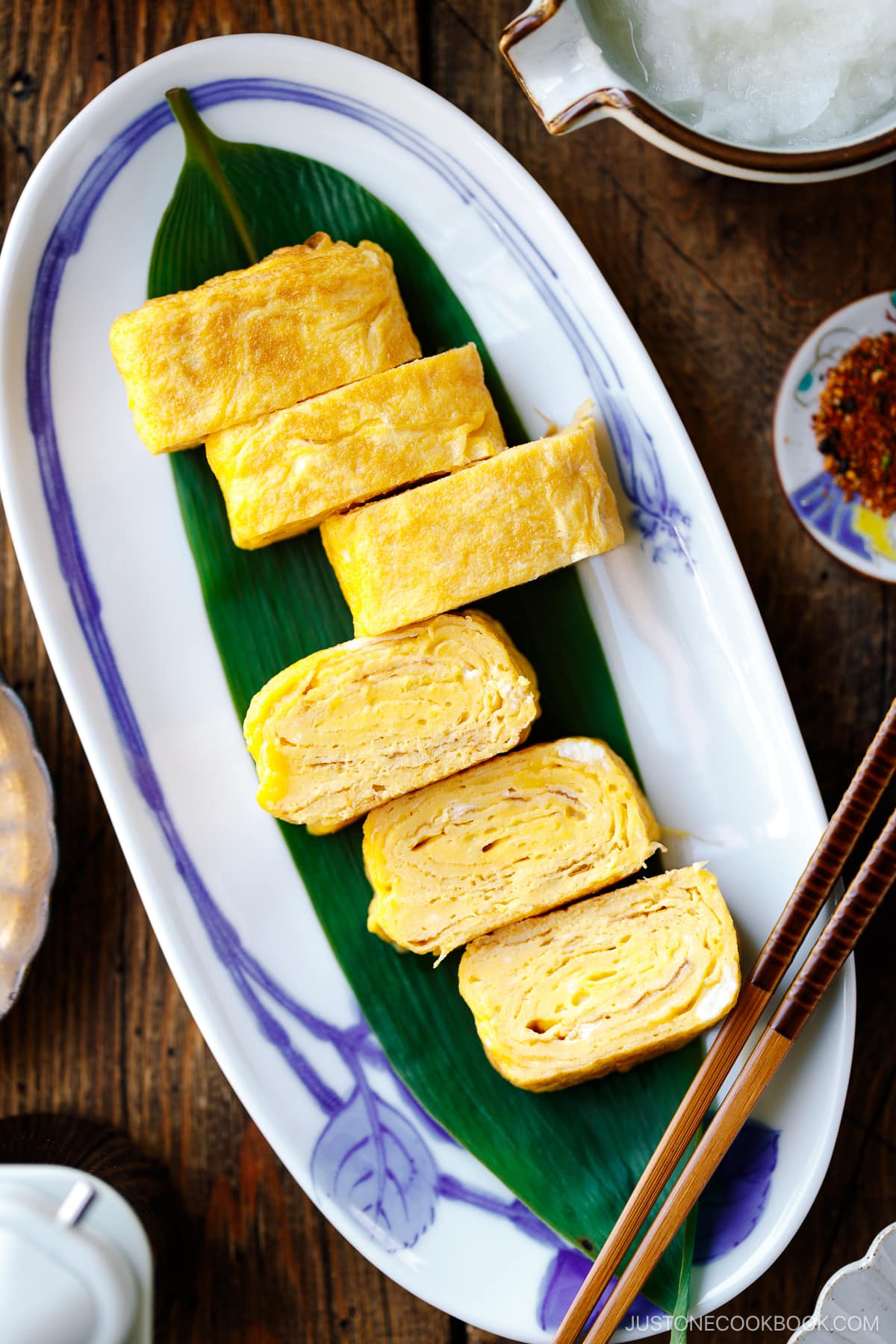 An oval Japanese plate containing Japanese rolled omelette, Tamagoyaki, placed over a bamboo leaf.