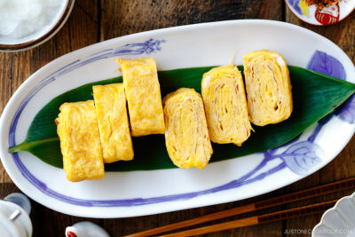 An oval Japanese plate containing Japanese rolled omelette, Tamagoyaki, placed over a bamboo leaf.
