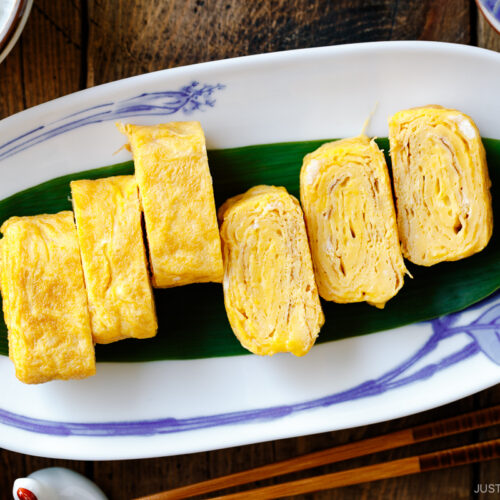 An oval Japanese plate containing Japanese rolled omelette, Tamagoyaki, placed over a bamboo leaf.