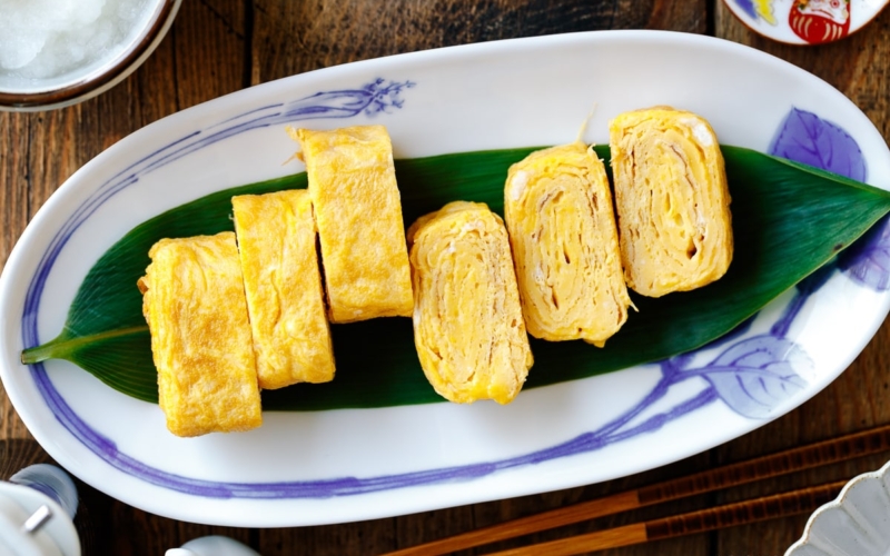 An oval Japanese plate containing Japanese rolled omelette, Tamagoyaki, placed over a bamboo leaf.