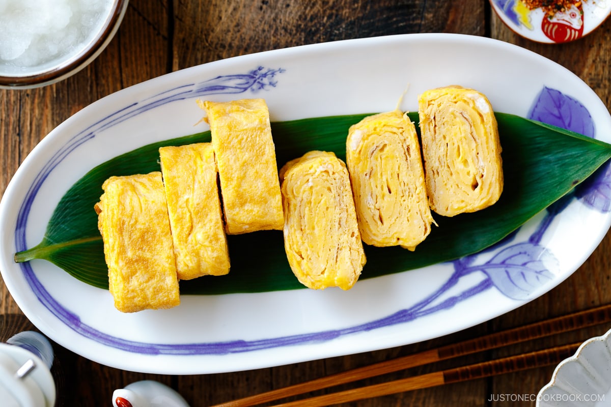 An oval Japanese plate containing Japanese rolled omelette, Tamagoyaki, placed over a bamboo leaf.