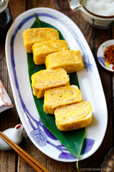 An oval Japanese plate containing Japanese rolled omelette, Tamagoyaki, placed over a bamboo leaf.