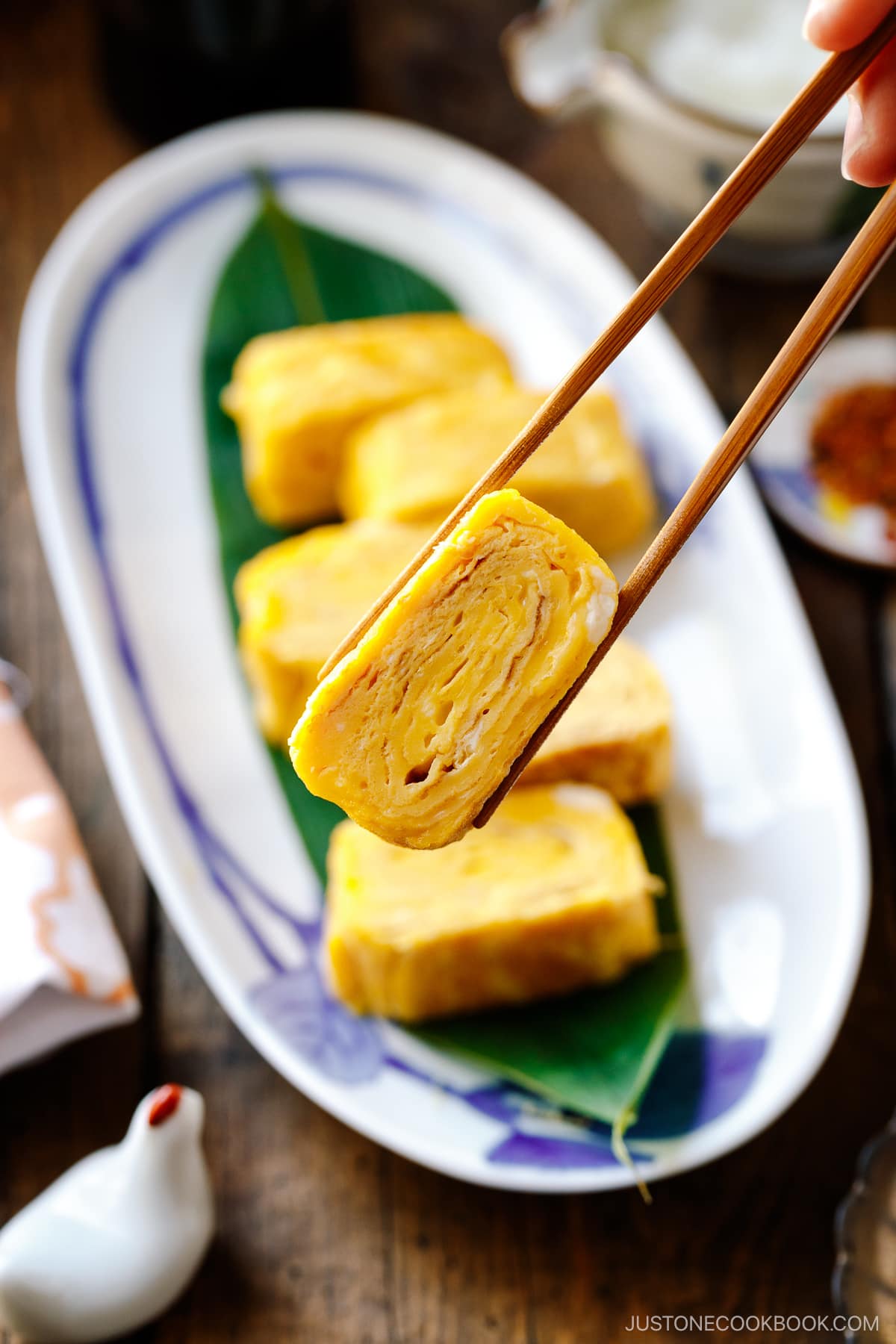 An oval Japanese plate containing Japanese rolled omelette, Tamagoyaki, placed over a bamboo leaf.