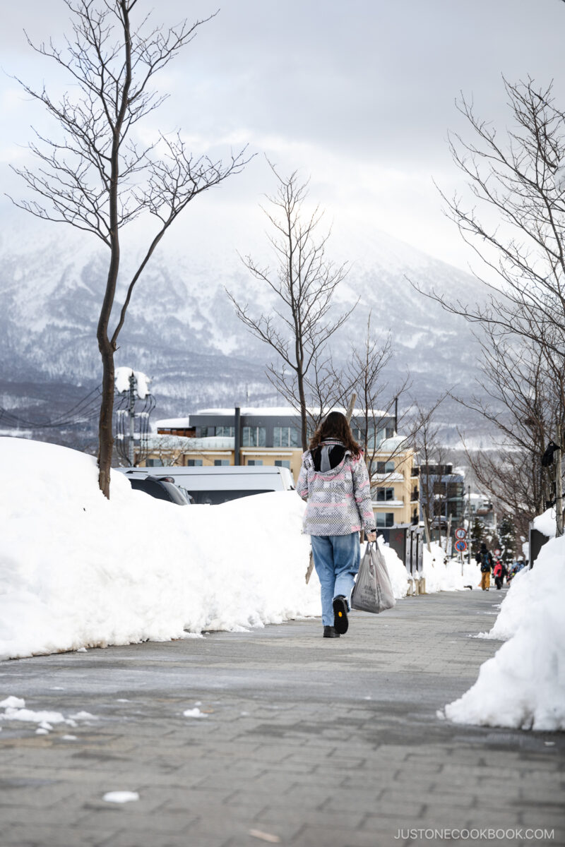 Person carrying shopping walking down Grand Hirafu road with Mt Yotei in the background