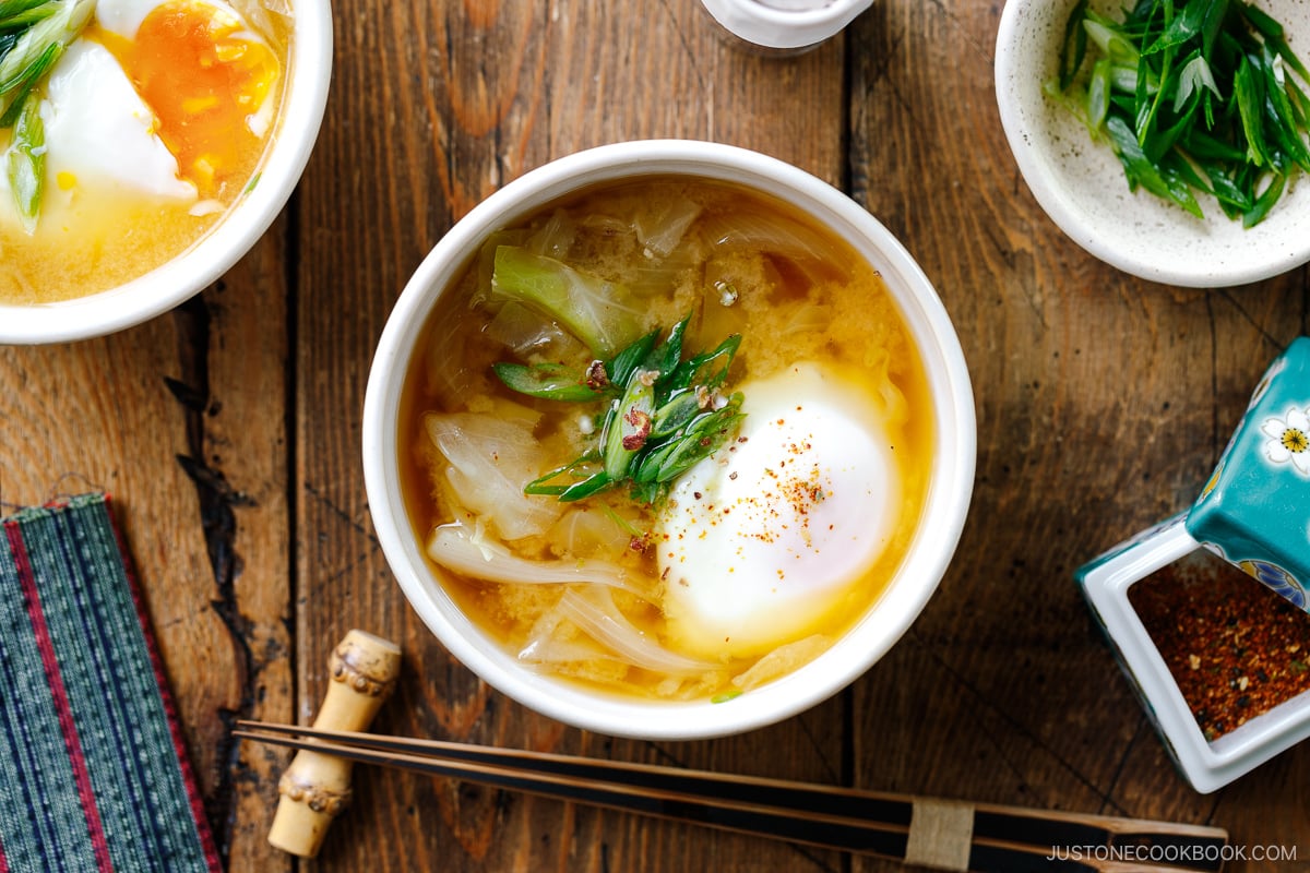 White ceramic bowls containing Cabbage and Onsen Tamago Miso Soup topped with green onions and shichimi togarashi.