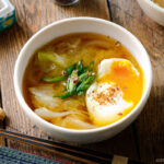 White ceramic bowls containing Cabbage and Onsen Tamago Miso Soup topped with green onions and shichimi togarashi.