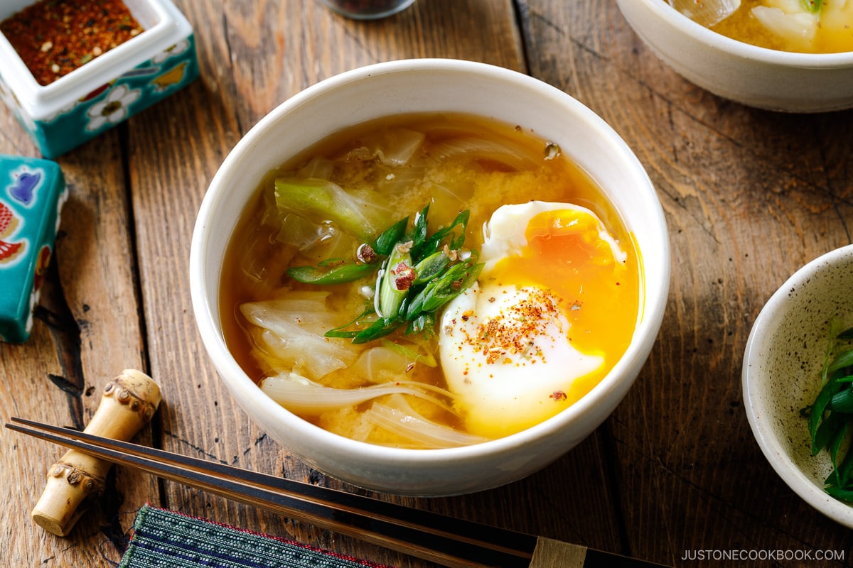 White ceramic bowls containing Cabbage and Onsen Tamago Miso Soup topped with green onions and shichimi togarashi.