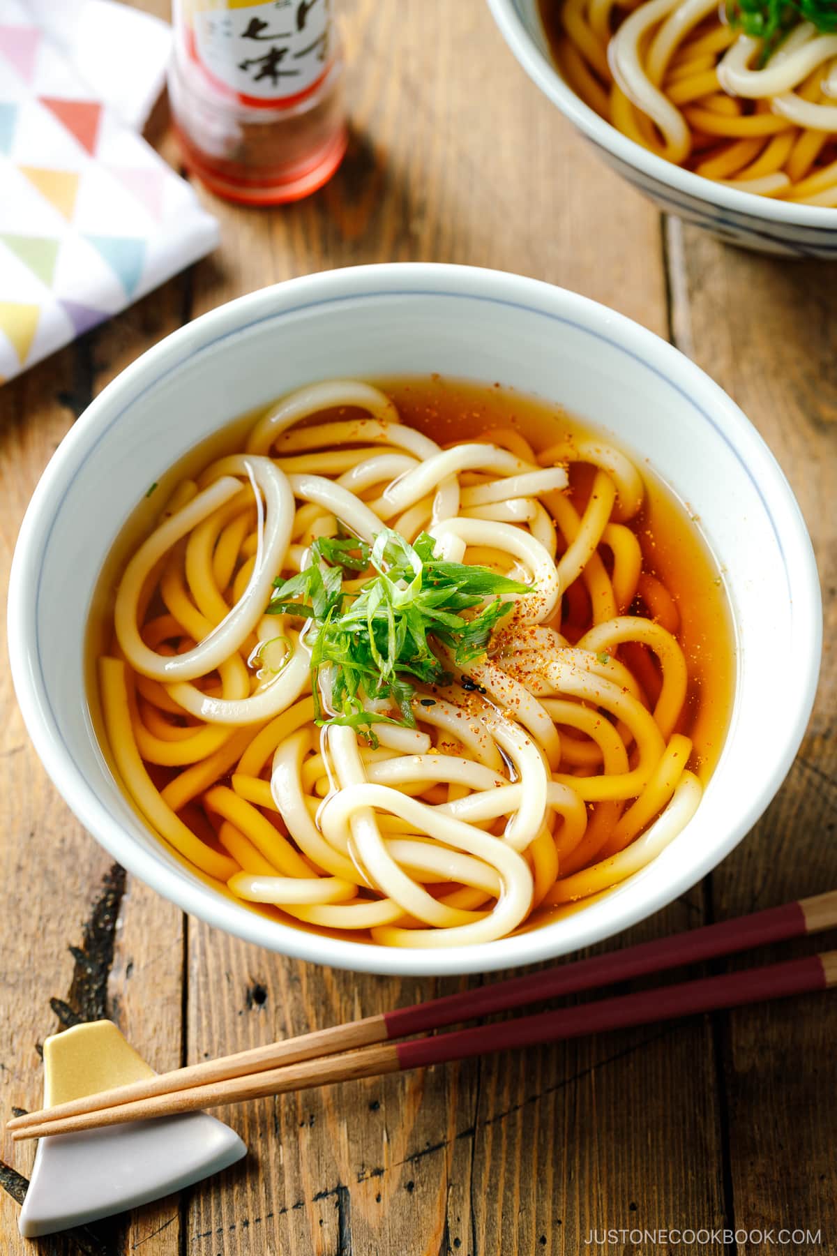 Japanese bowls containing Classic Udon Noodle Soup called Kake Udon or Su Udon, topped with sliced green onion and shichimi togarashi (Japanese seven spice).