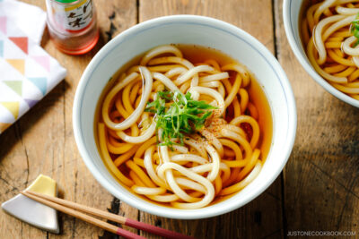 Japanese bowls containing Classic Udon Noodle Soup called Kake Udon or Su Udon, topped with sliced green onion and shichimi togarashi (Japanese seven spice).