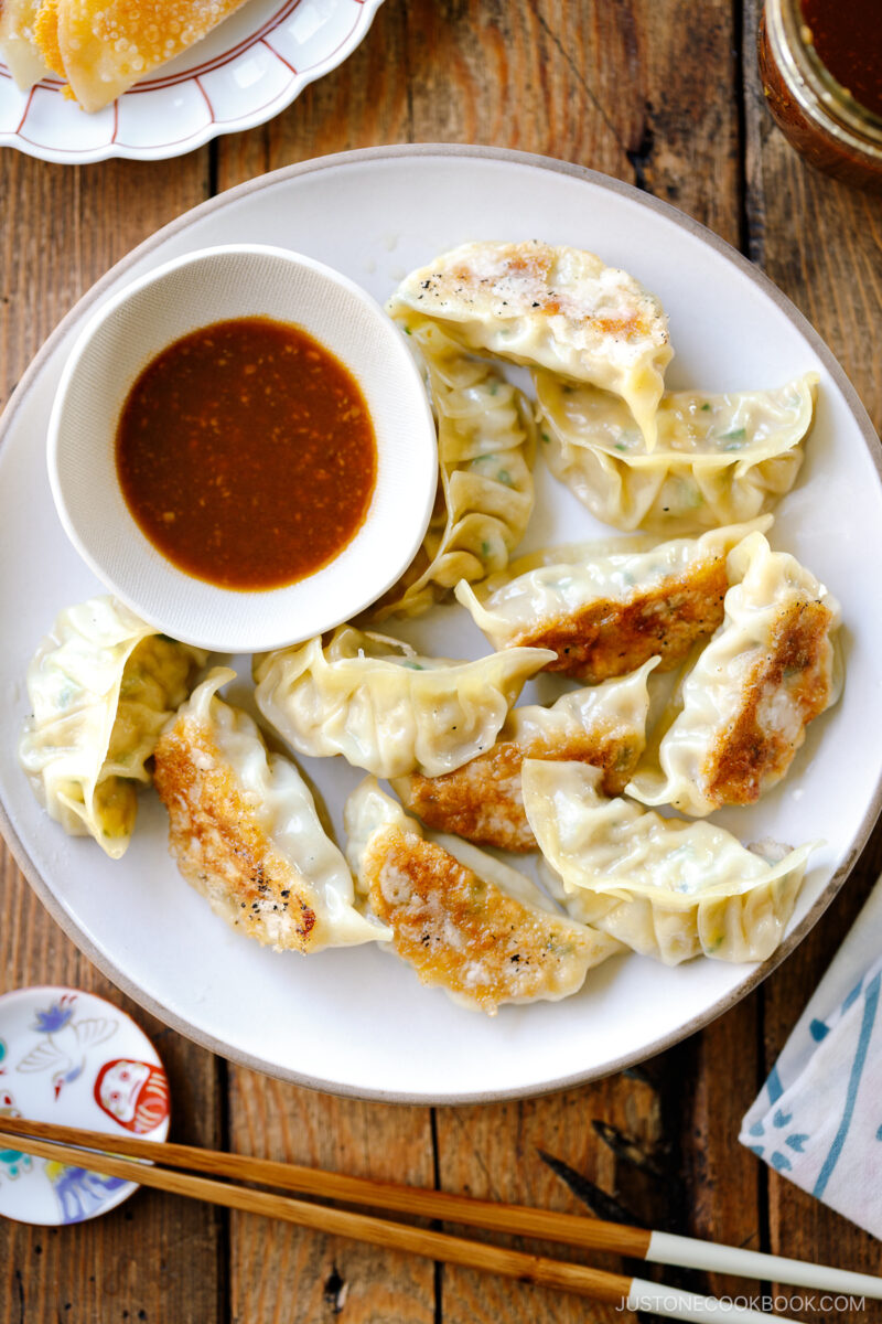 A round plate containing Japanese pan-fried dumplings, Napa Cabbage Gyoza, served with a savory miso dumpling sauce.