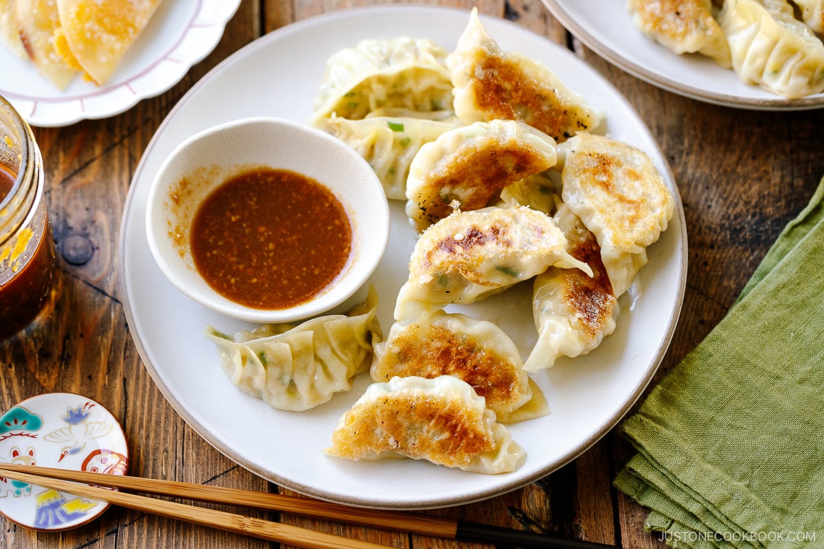 A round plate containing Japanese pan-fried dumplings, Napa Cabbage Gyoza, served with a savory miso dumpling sauce.