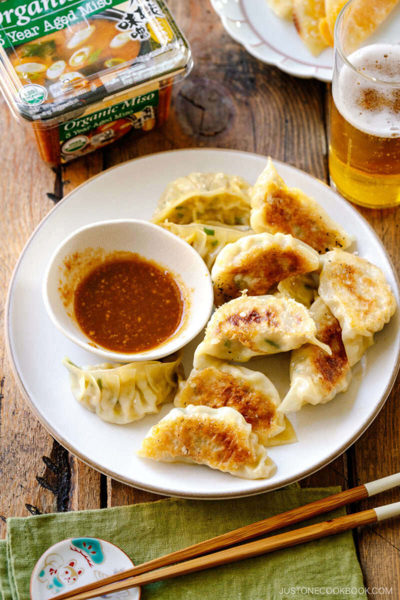 A round plate containing Japanese pan-fried dumplings, Napa Cabbage Gyoza, served with a savory miso dumpling sauce.