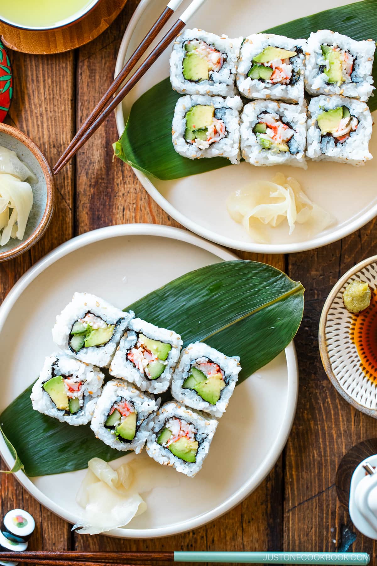 Round ceramic plates containing six pieces of California rolls over a bamboo leaf along with sushi ginger.