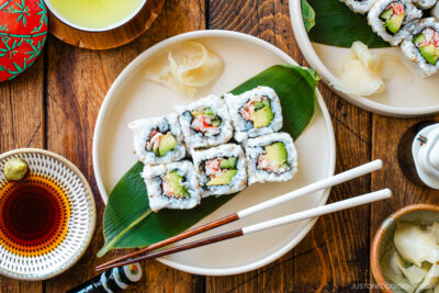 Round ceramic plates containing six pieces of California rolls over a bamboo leaf along with sushi ginger.