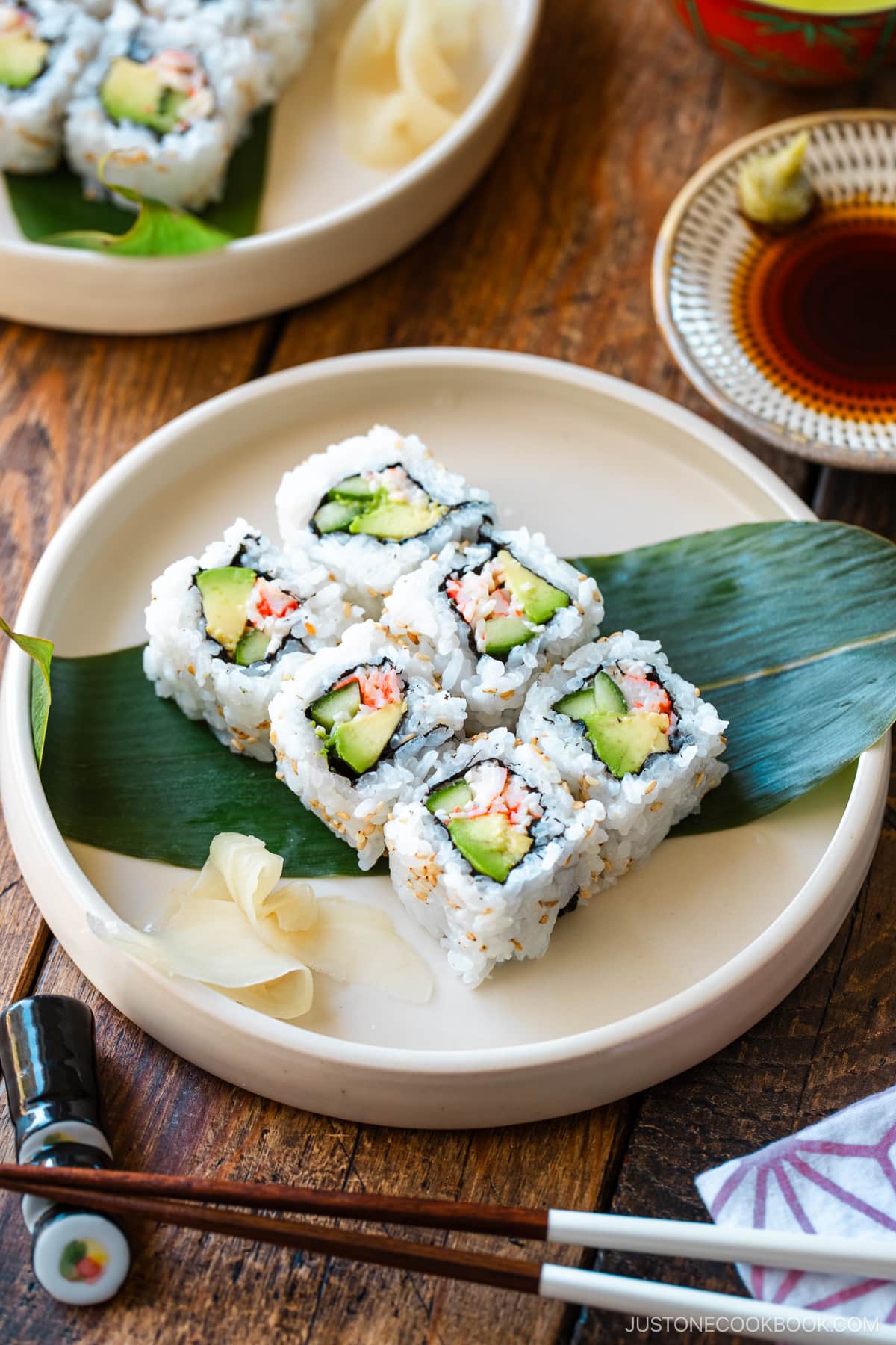 Round ceramic plates containing six pieces of California rolls over a bamboo leaf along with sushi ginger.