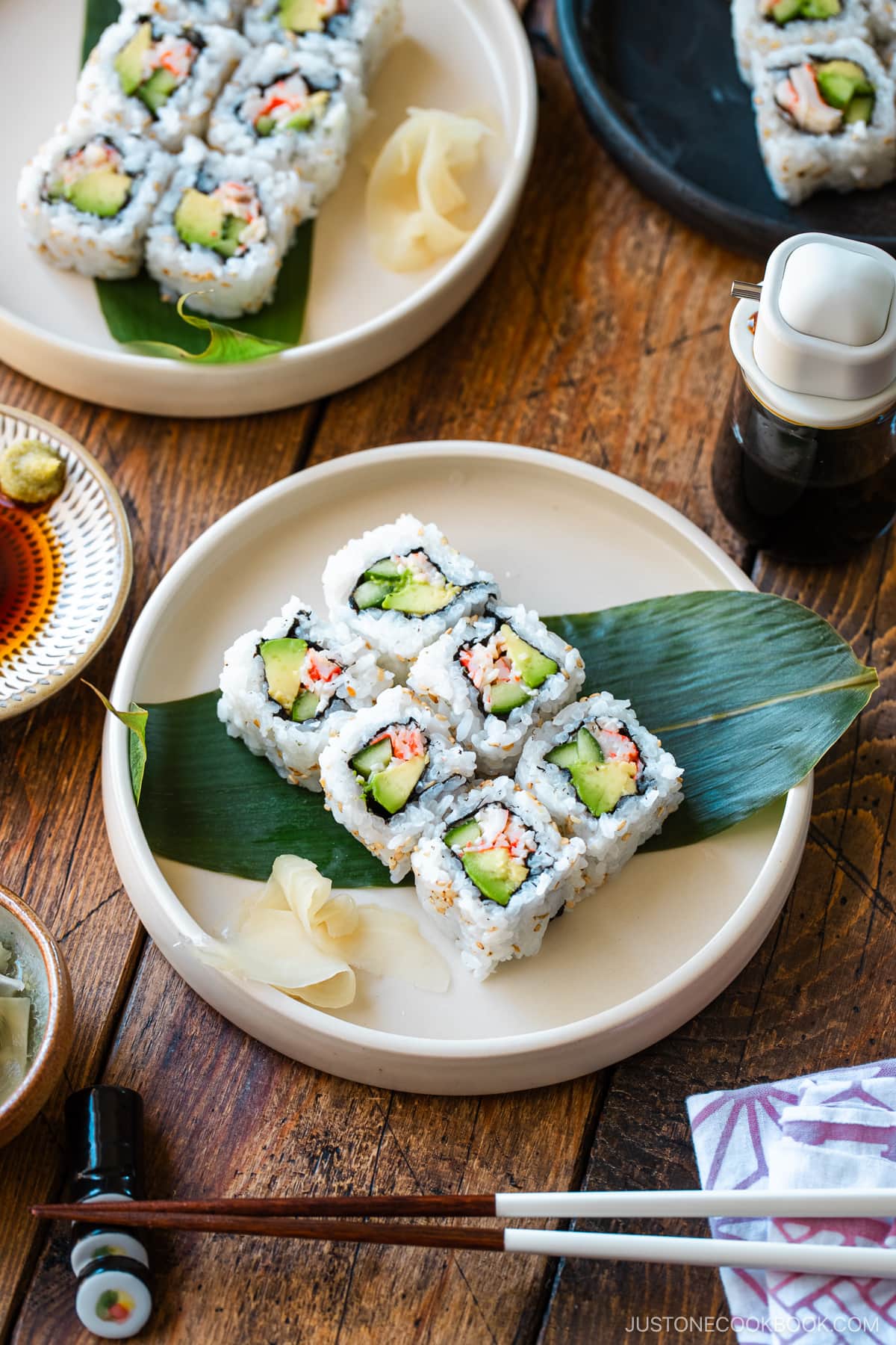 Round ceramic plates containing six pieces of California rolls over a bamboo leaf along with sushi ginger.