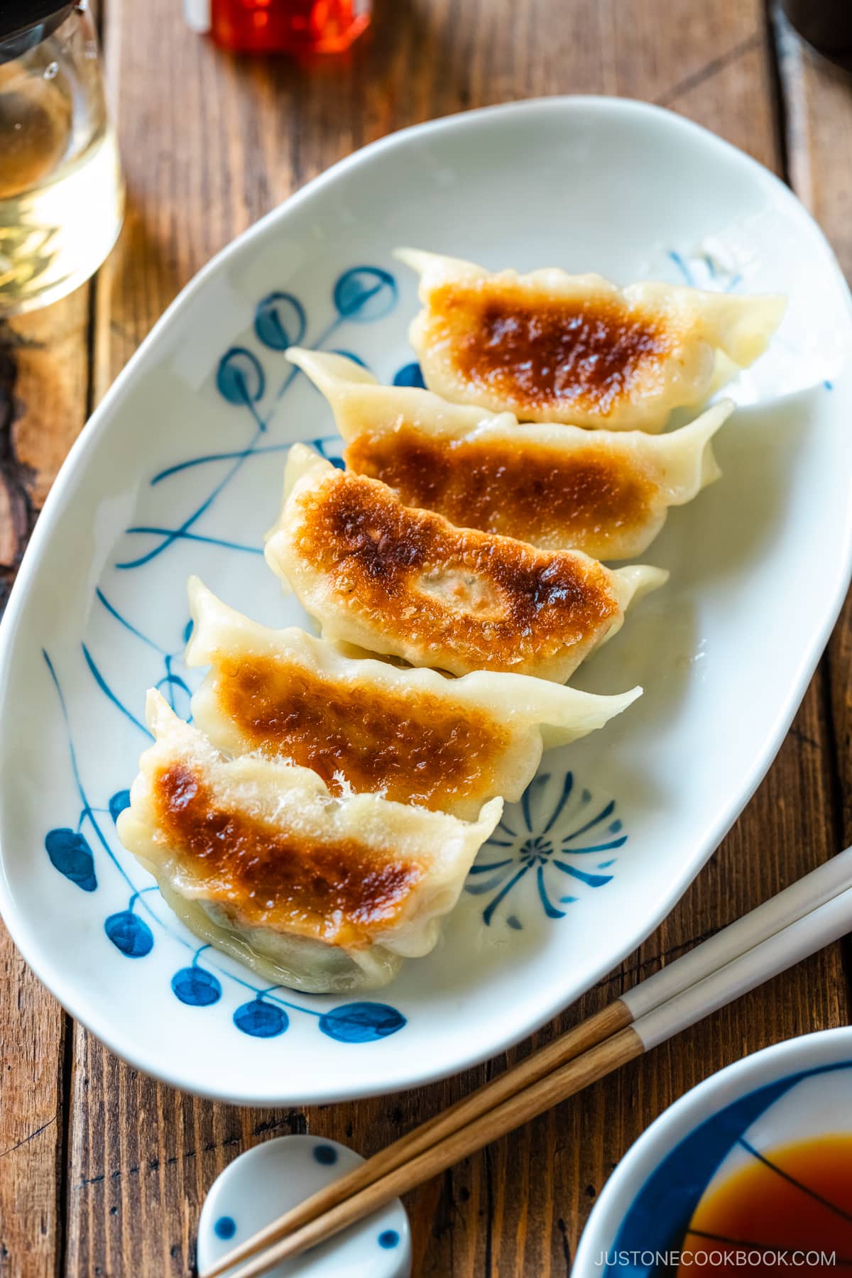 An oval plate containing gyoza (Japanese potstickers or pan-fried dumplings) with a small plate of dipping sauce made with soy sauce, vinegar, and Japanese chili oil.