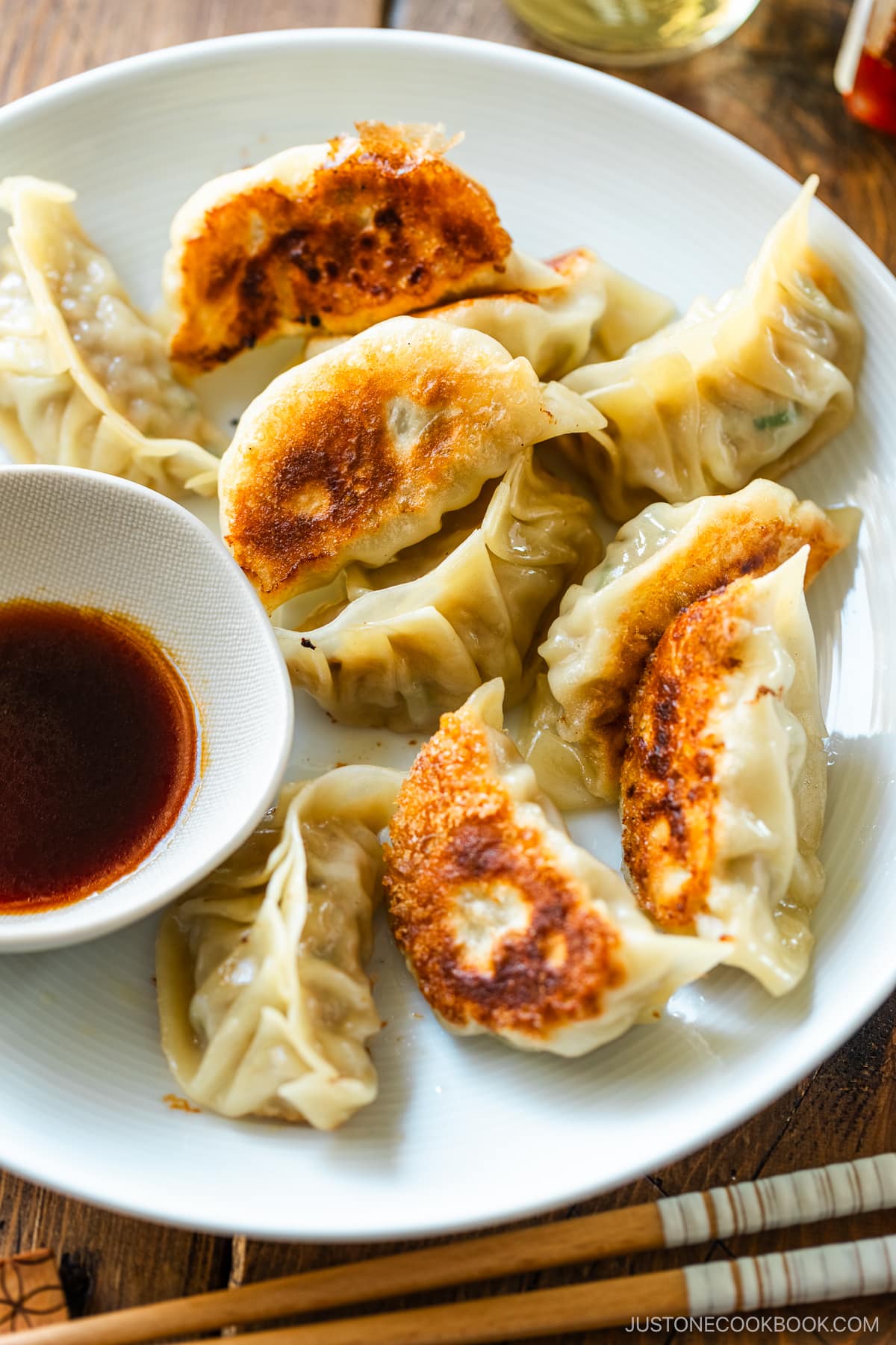A round plate containing gyoza (Japanese potstickers or pan-fried dumplings) with a small plate of dipping sauce made with soy sauce, vinegar, and Japanese chili oil.