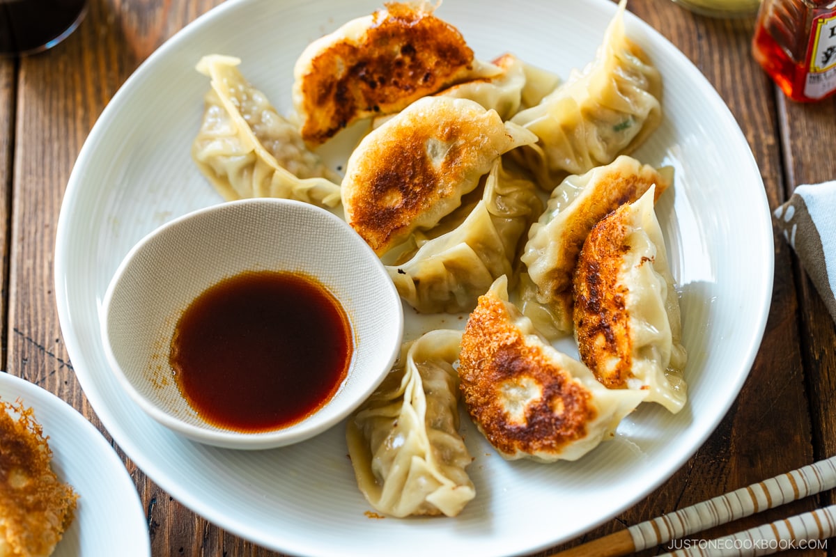 A round plate containing gyoza (Japanese potstickers or pan-fried dumplings) with a small plate of dipping sauce made with soy sauce, vinegar, and Japanese chili oil.