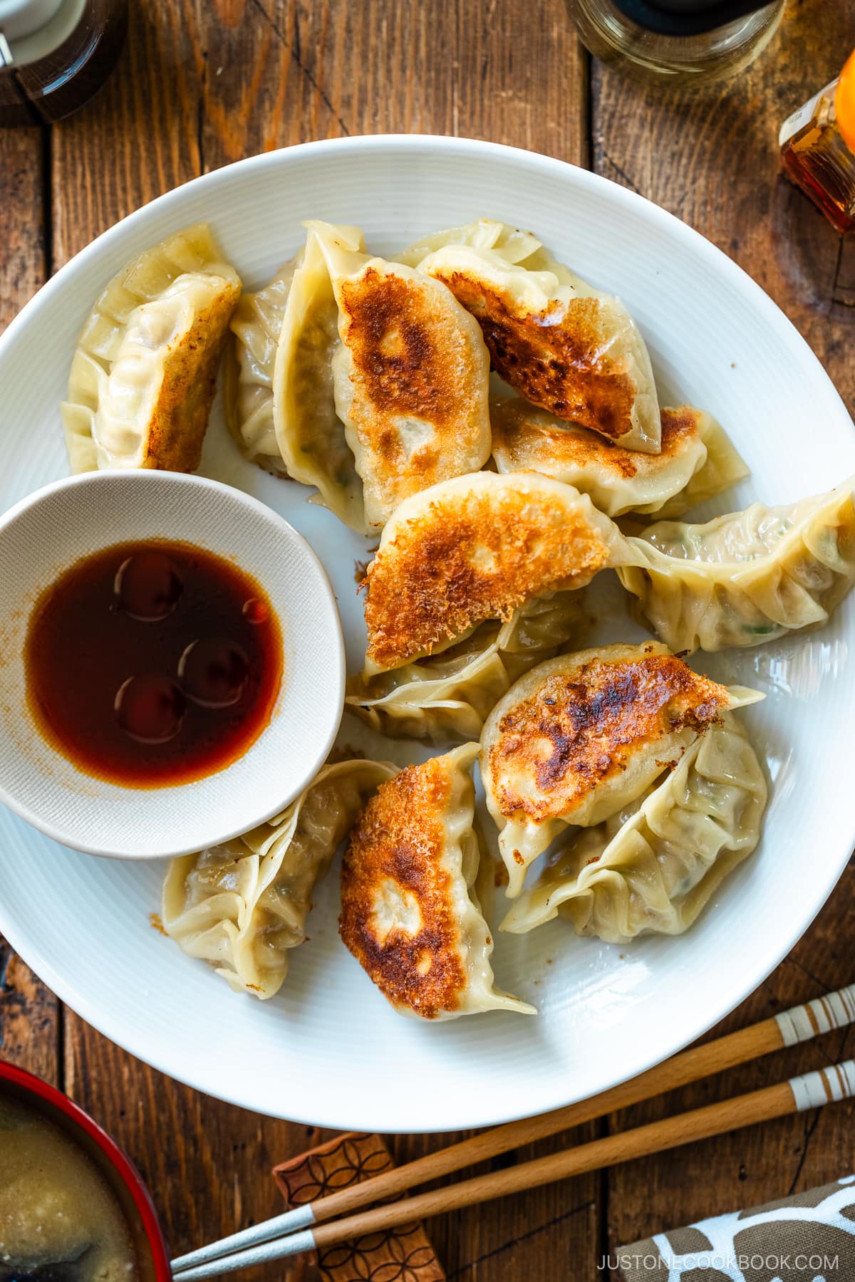 A round plate containing gyoza (Japanese potstickers or pan-fried dumplings) with a small plate of dipping sauce made with soy sauce, vinegar, and Japanese chili oil.