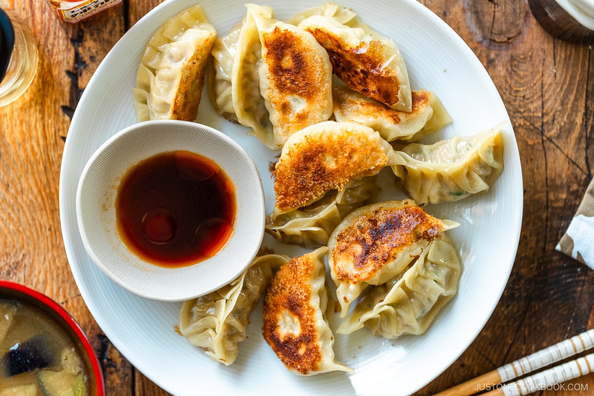 A round plate containing gyoza (Japanese potstickers or pan-fried dumplings) with a small plate of dipping sauce made with soy sauce, vinegar, and Japanese chili oil.