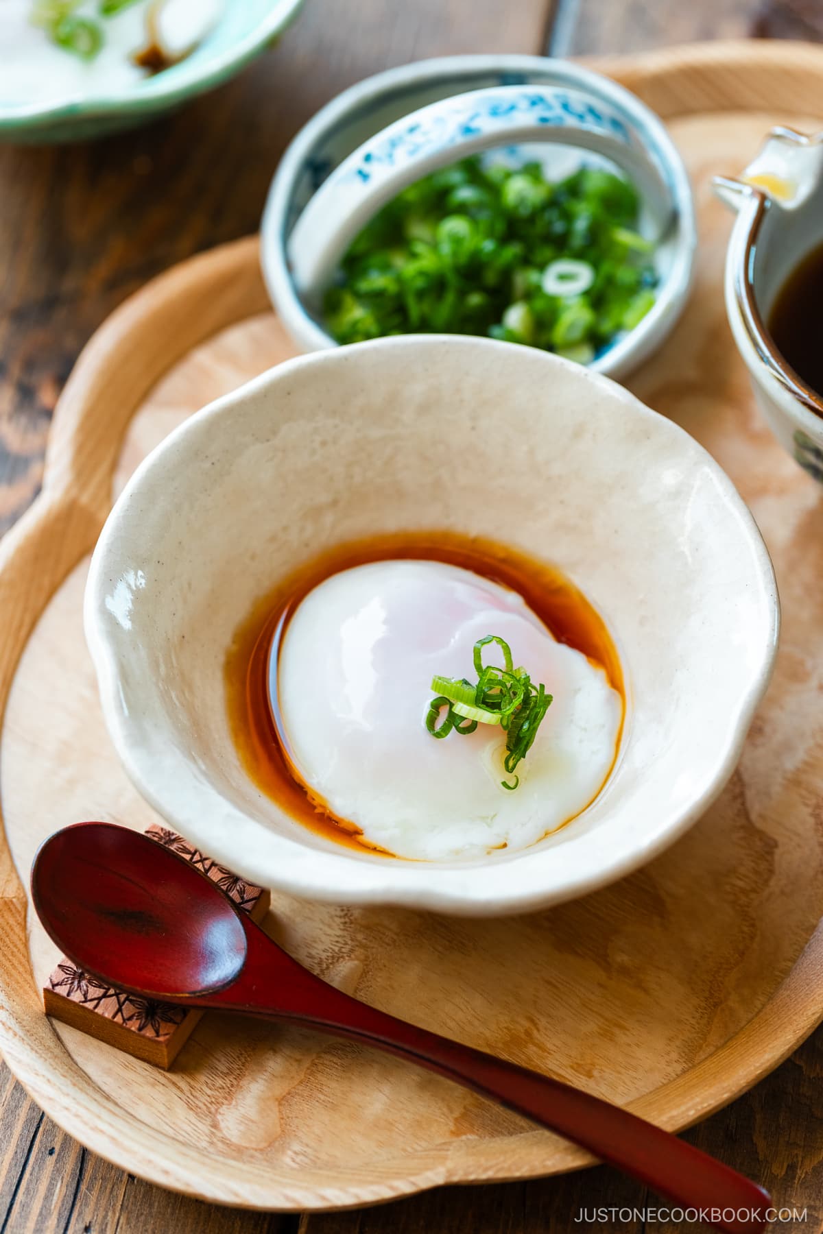 A white bowl containing Onsen Tamago (Japanese Hot Spring Egg) drizzled with dashi-based broth and garnished with sliced green onion.