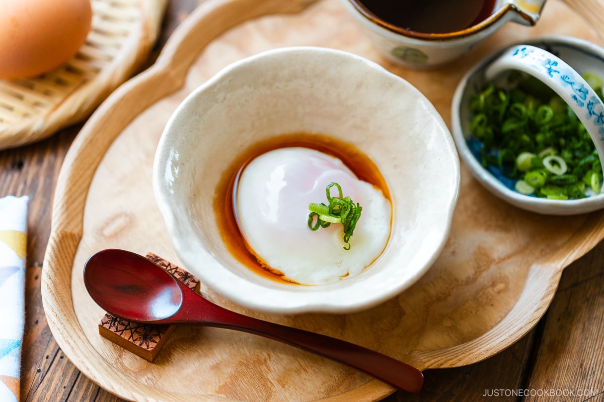 A white bowl containing Onsen Tamago (Japanese Hot Spring Egg) drizzled with dashi-based broth and garnished with sliced green onion.