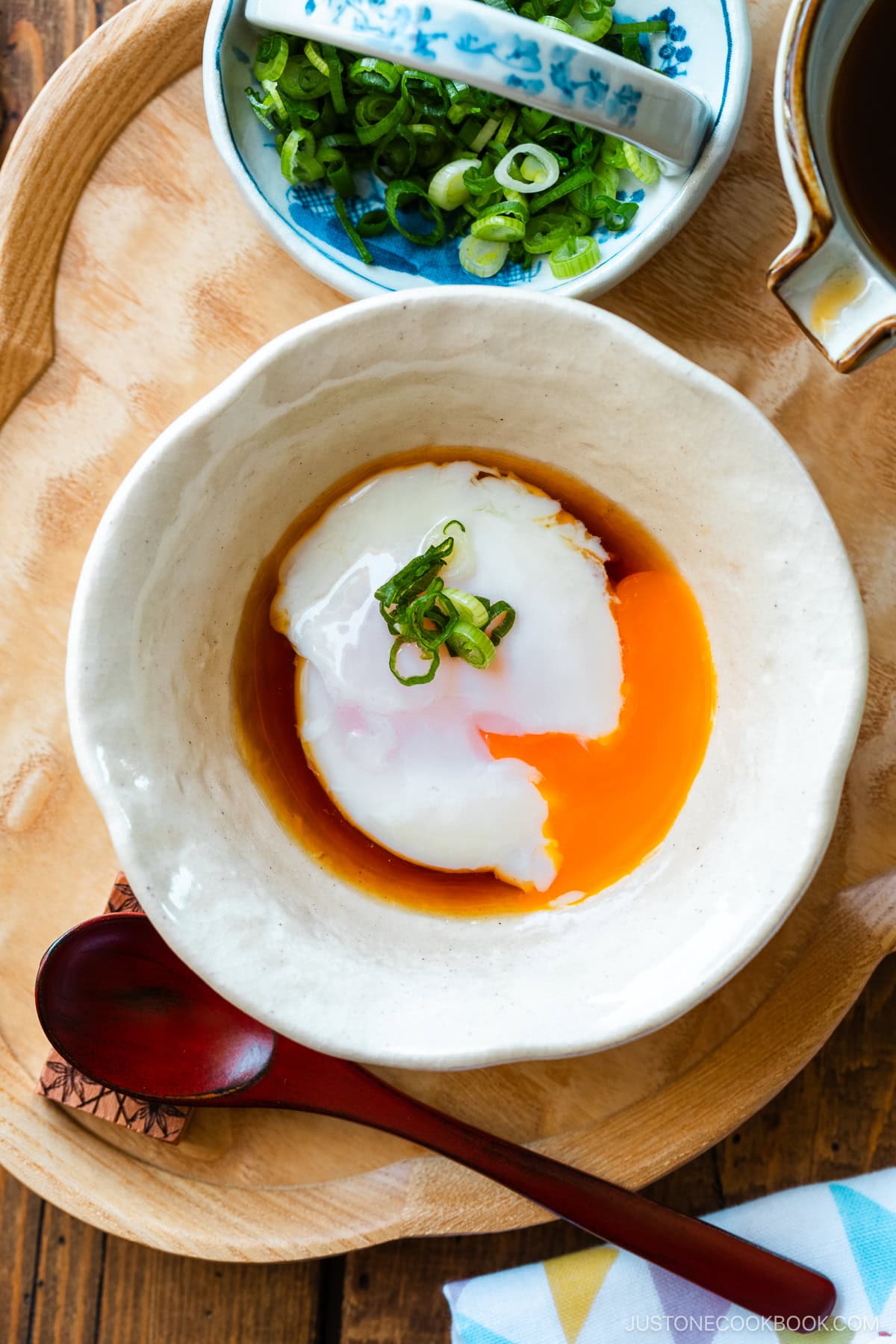 A white bowl containing Onsen Tamago (Japanese Hot Spring Egg) drizzled with dashi-based broth and garnished with sliced green onion.