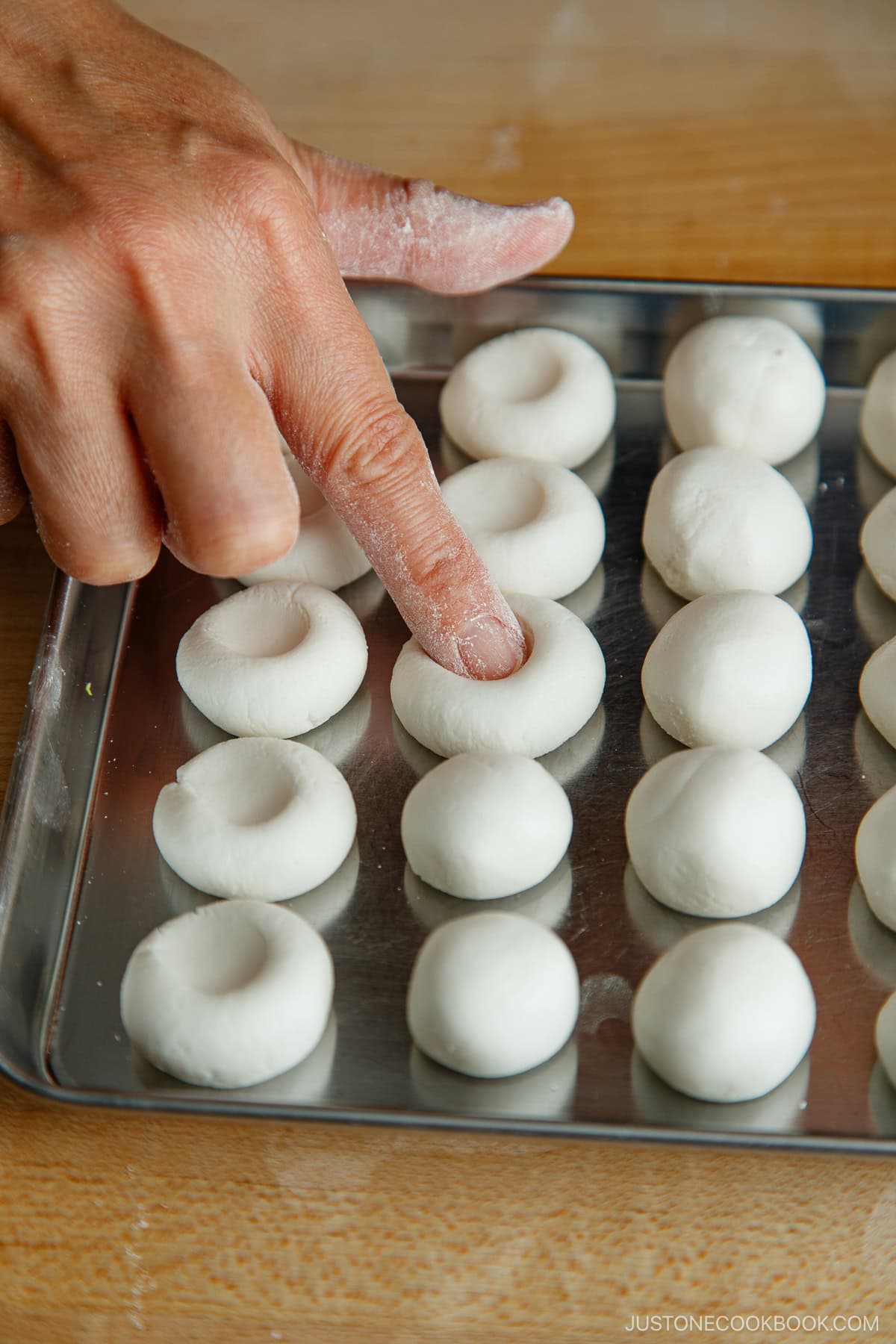 A finger pressing shiratama dango (mochi balls) lined up on a prep tray.