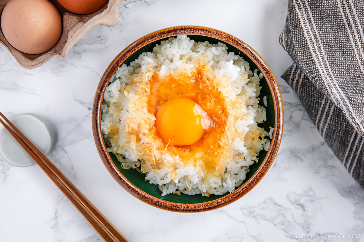 A bowl containing steamed rice, raw egg, sprinkled katsuobushi, and a drizzle of soy sauce.