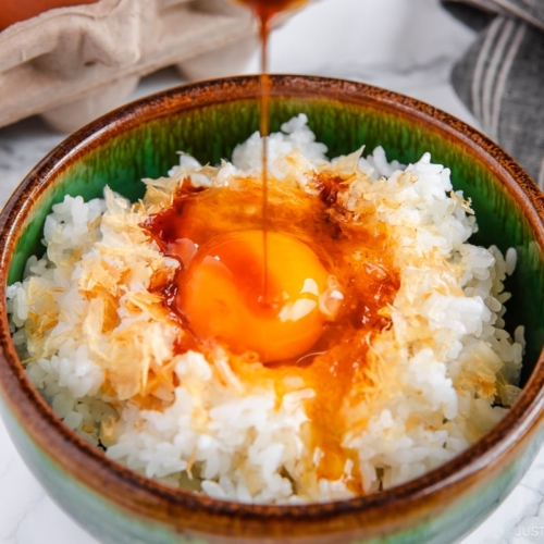 A bowl containing steamed rice, raw egg, sprinkled katsuobushi, and a drizzle of soy sauce.